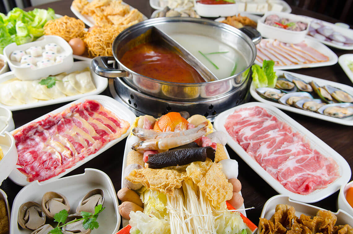 A selection of Chinese hot pot meats and vegetables surround the table