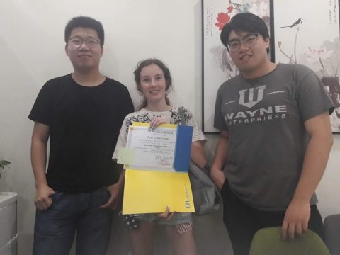 Perle holding up her HSK certificate next to her two teachers